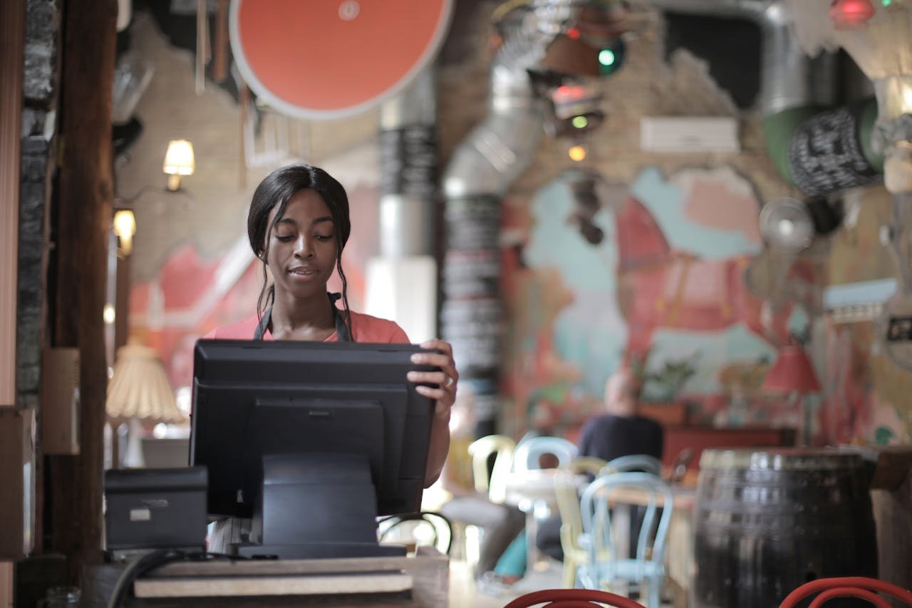 Black woman operating point of sale system in a vibrant restaurant ambiance.